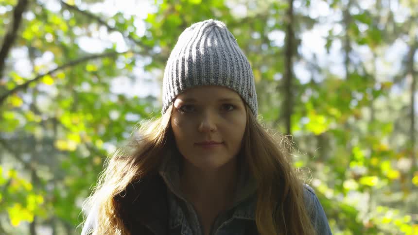 A woman with a denim jacket and a hat standing in the forest