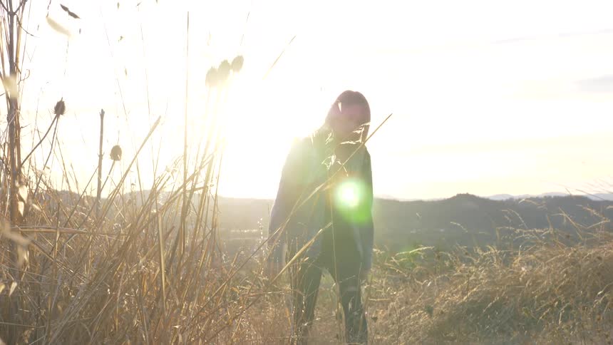 A woman is walking through a grassland area