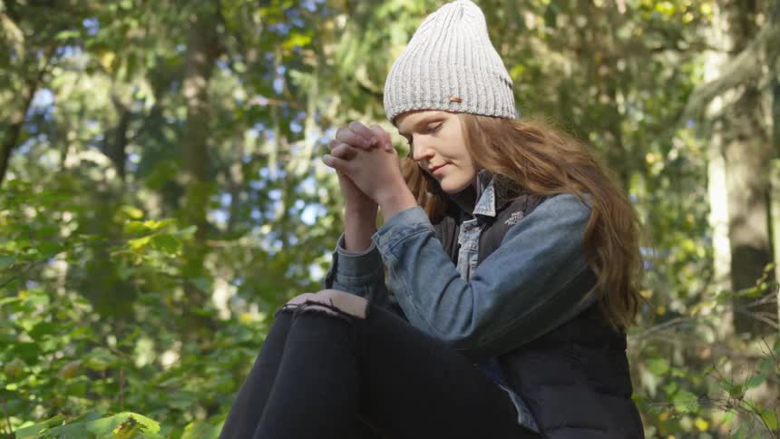 A young woman sits in the woods and prays