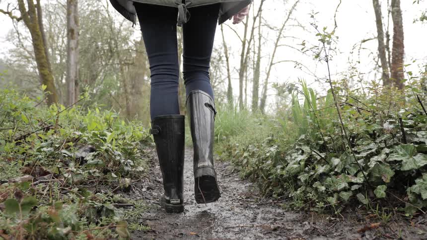 A woman with black boots walking in a muddy path walk in the rain