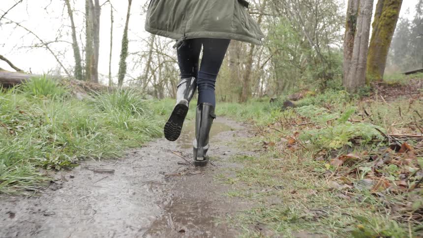 A woman splashes in muddy puddles while running outside in the rain