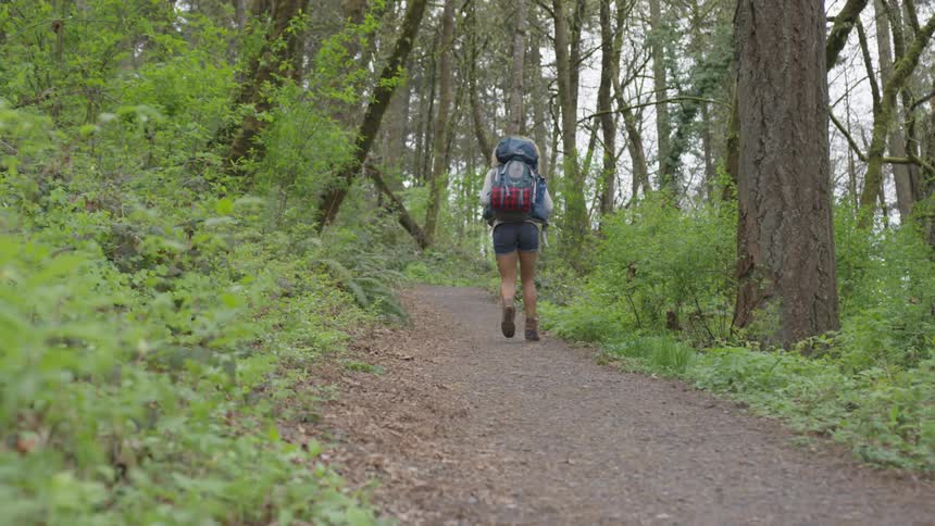 A woman walking up a path in a forest wearing a large backpack