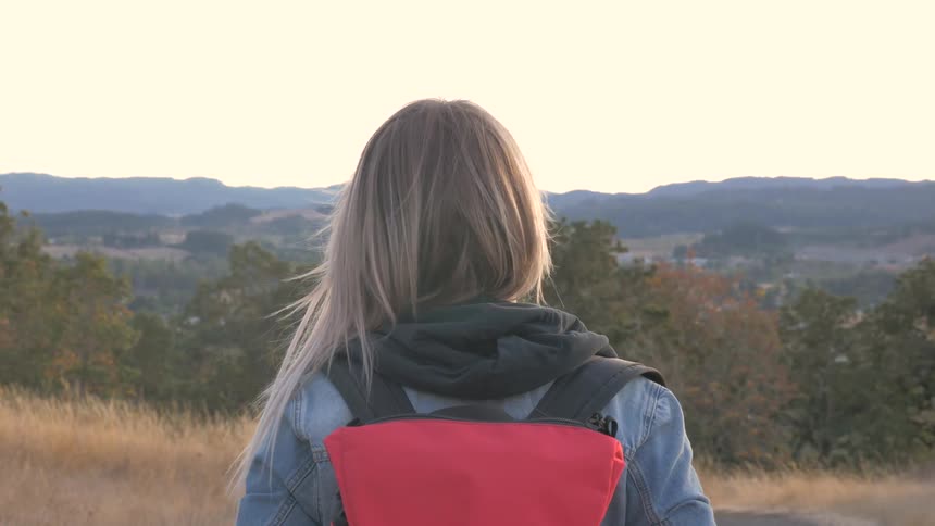A woman stands looking at a mountain range in the distance