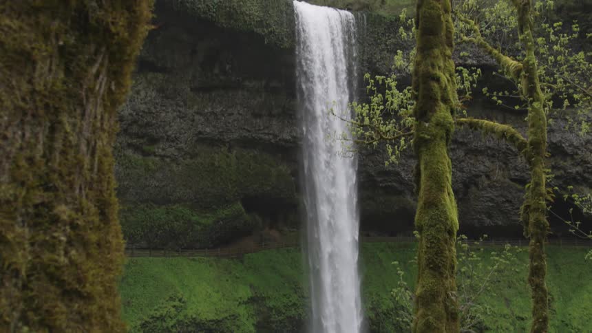 A waterfall flows over a mossy cliff into a pool of water below
