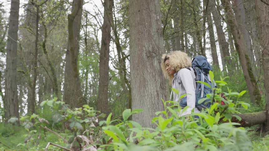 Black woman wearing a backpack and hiking in the middle of a forest
