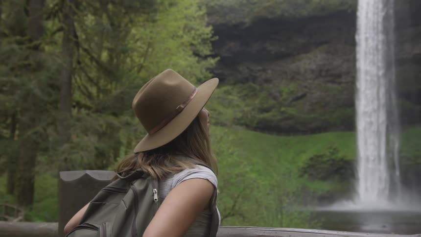 Woman in a fedora gazing up at a waterfall