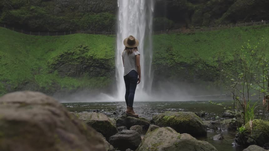 A woman standing on a rock staring at a waterfall