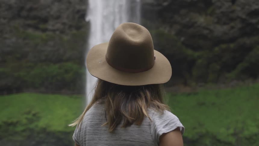 Woman in hat faces tall waterfall
