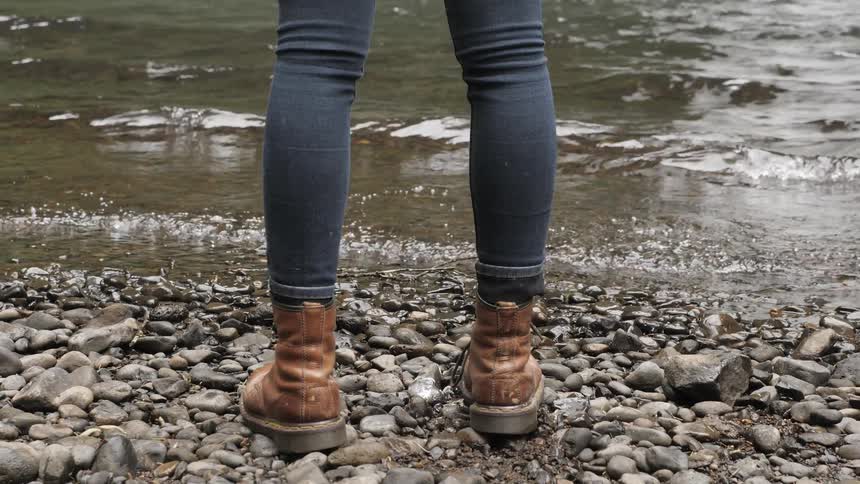 A woman in boots standing on a rocky shore