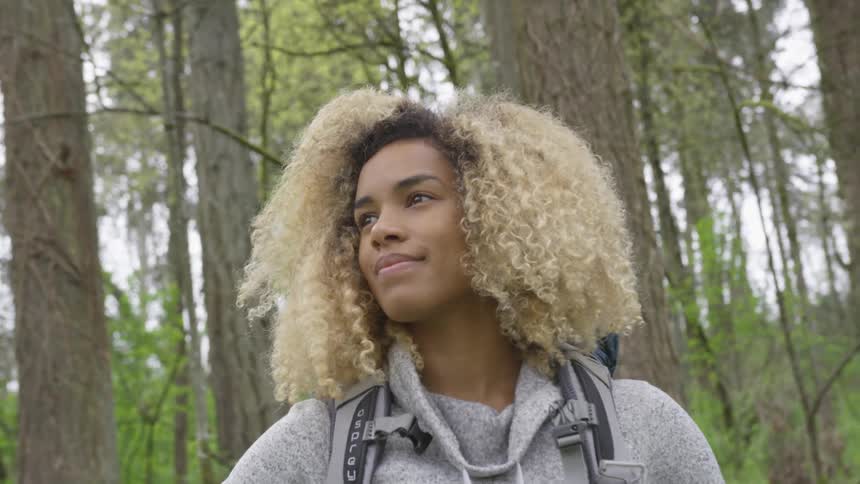A woman stands in a forest and smiles