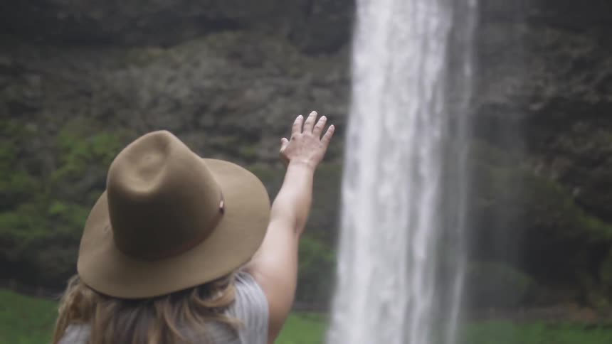 White woman saluting a waterfall in the middle of a forest