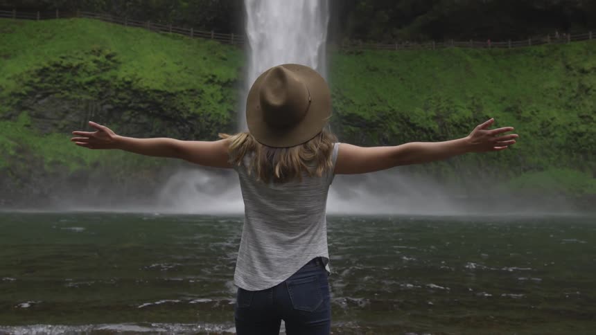 Woman standing with arms wide open in front of a waterfall