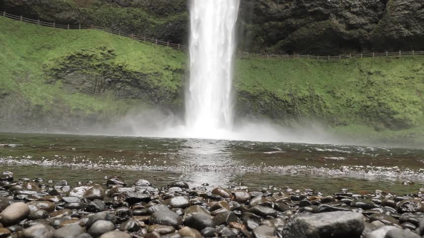 A waterfall pours into a body of water and waves ripple forward