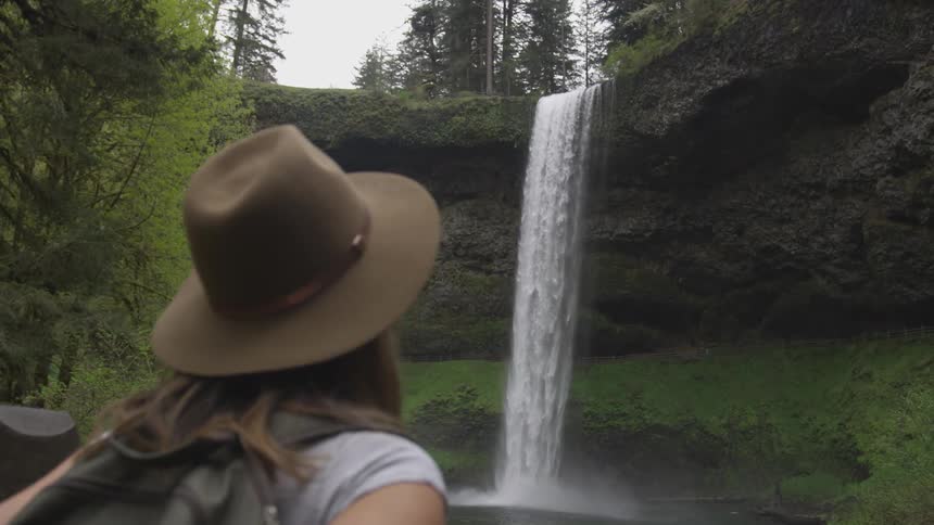 A woman looks up at a waterfall