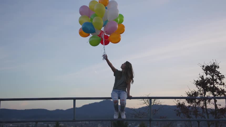 Woman sits on rail holding a bunch of balloons