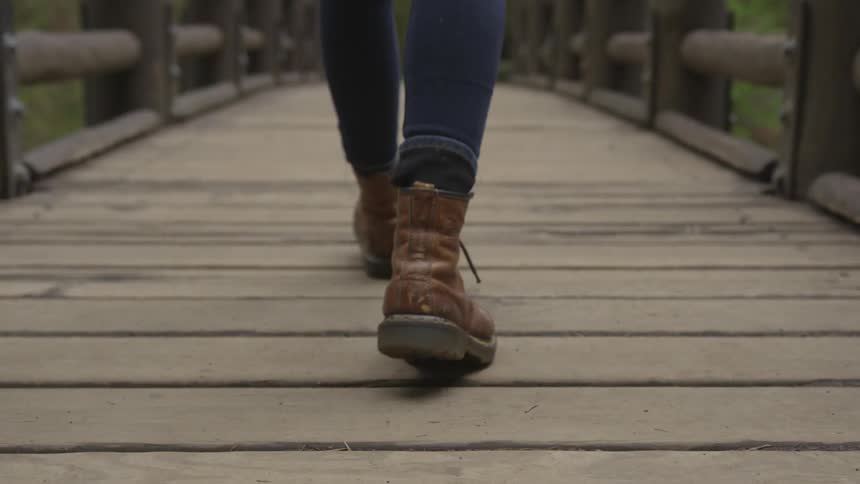 Person in brown boots walking across a narrow wooden bridge