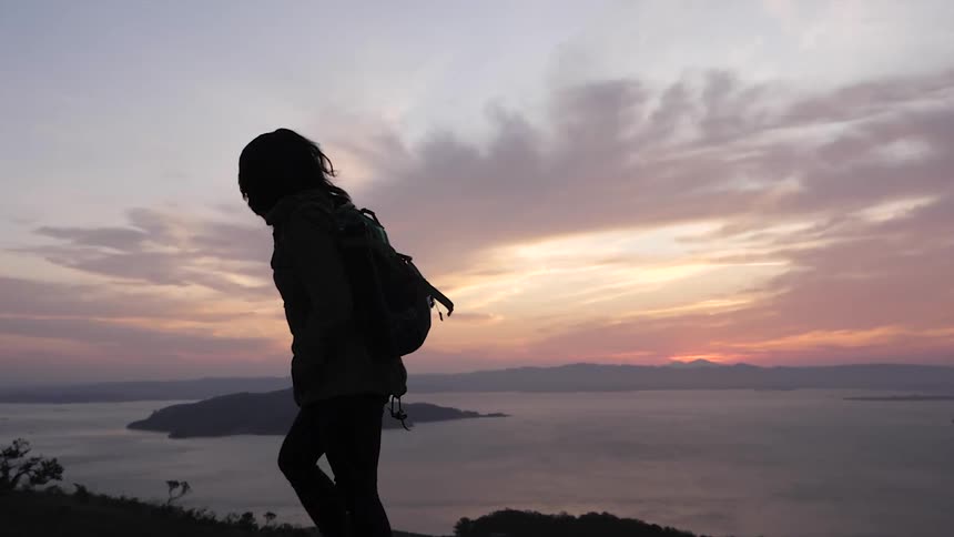 A silhouetted person hikes next to a lake at sunset