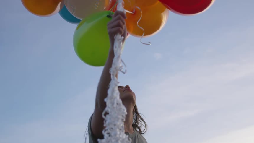 A young white woman holds a bundle of balloons