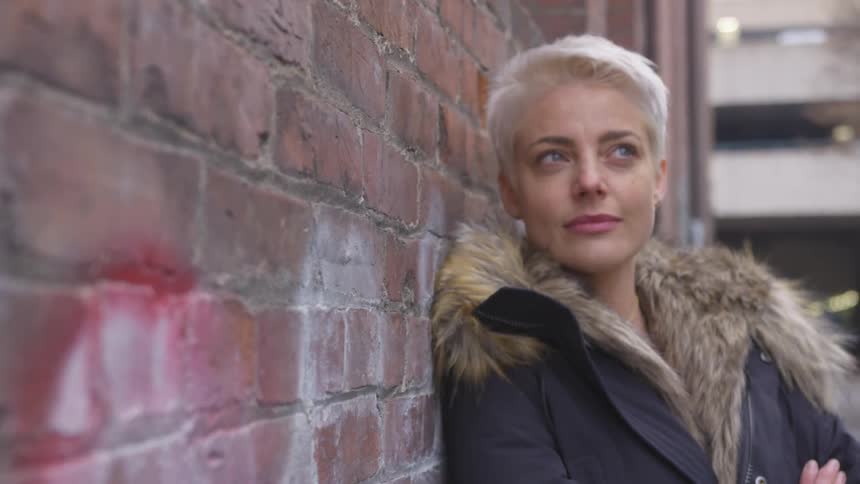 A woman leans against a brick wall