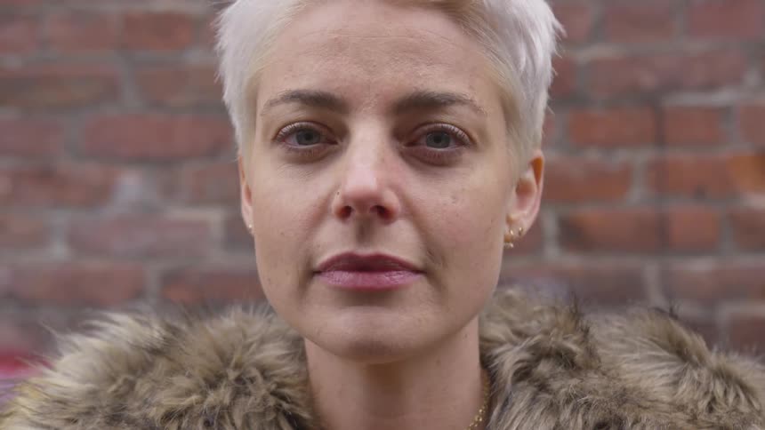 A woman with a fur coat standing with a brick wall in the background