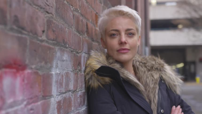 A woman leans against a brick wall while wearing a winter coat