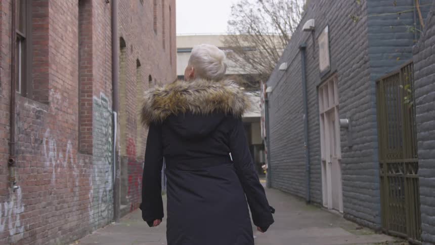 A white woman in a winter coat takes a stroll down an alley