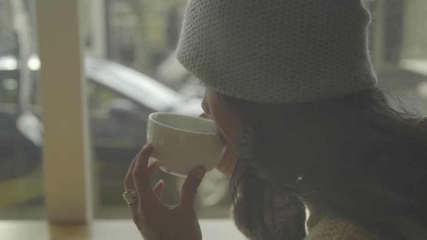 Woman wearing a toque drinks a hot beverage from a tea cup