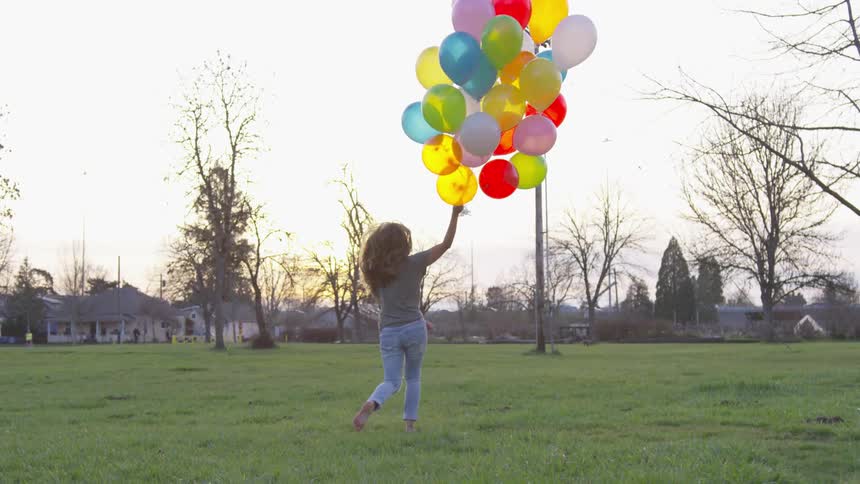 A woman runs through a field carrying a bundle of balloons
