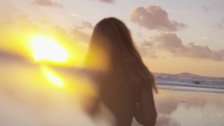 Woman touches her hair on the sand beach while the sun goes down