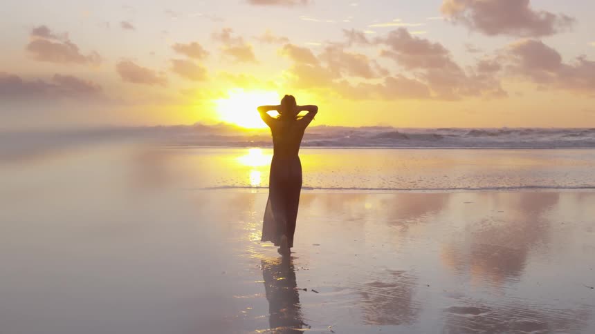 Woman walking at the beach next to the ocean at sunset