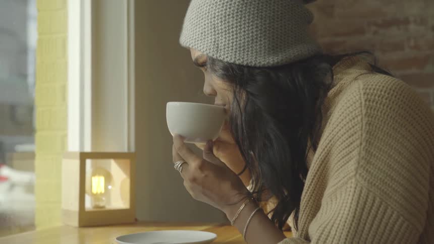 Woman in a cafe blows into her hot drink during the daytime
