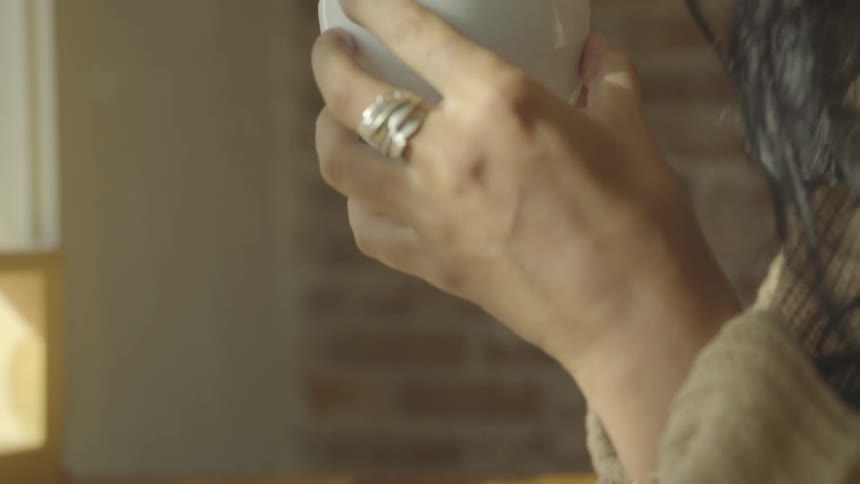 Girl wearing white wooly hat blows into hot drink and drinks in the daytime