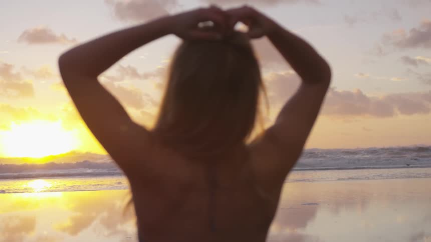 Woman looking at the horizon standing on a beach at sunset