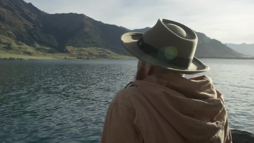 A bearded man sits at the shoreline