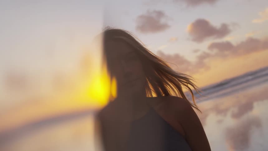 Blonde woman stands on the beach while the sun goes down