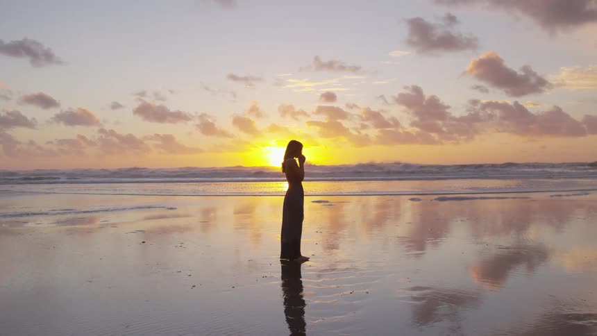 Woman standing at the shore of a beach at sunset