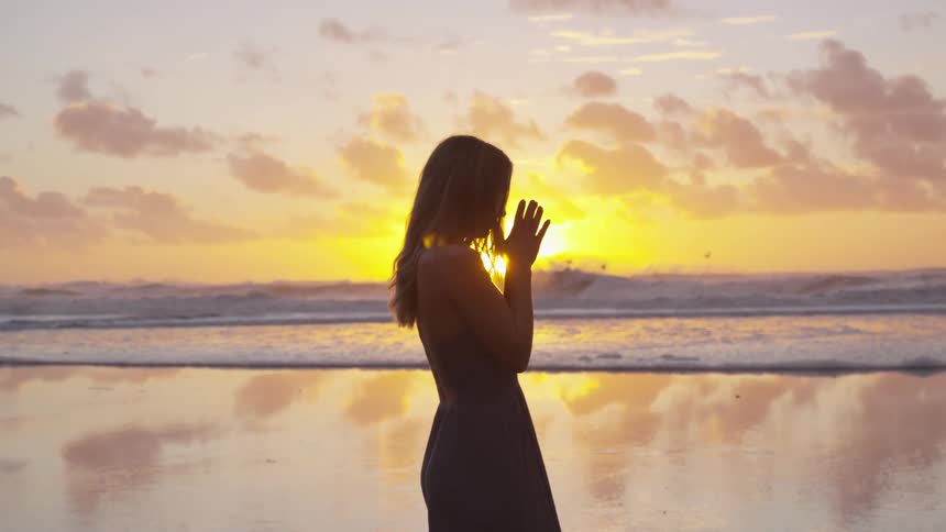 A woman stands with her hands together looking out at the water