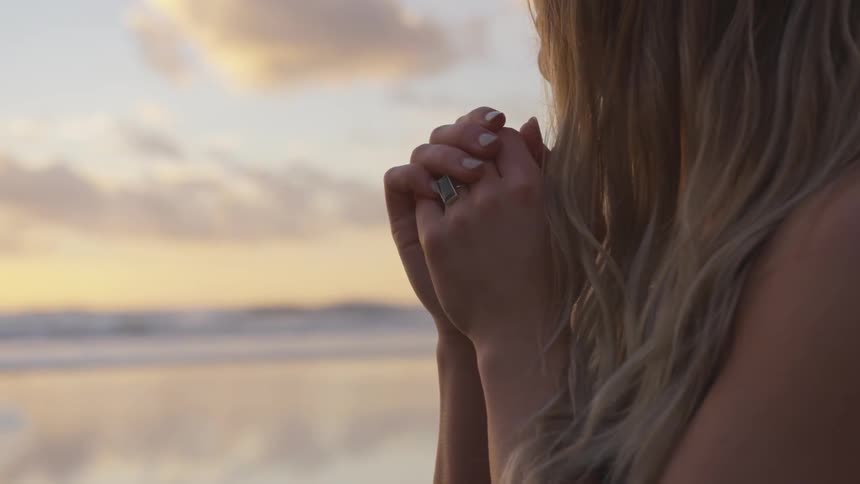 Blonde woman clasps hand on the beach next to the sea at sunset