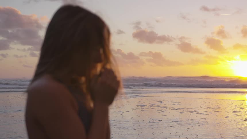Female standing with hands together near the shore at sunset