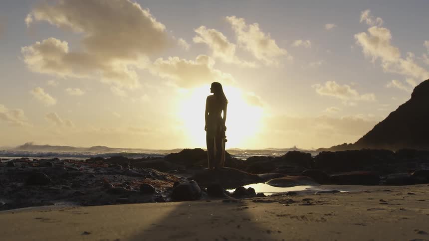 A woman standing on the rocks by the beach at sunset
