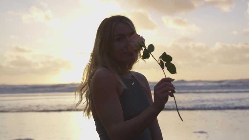 Woman standing on beach at sunset smells rose