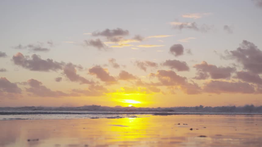 Ocean waves wash ashore a sandy beach at sunset