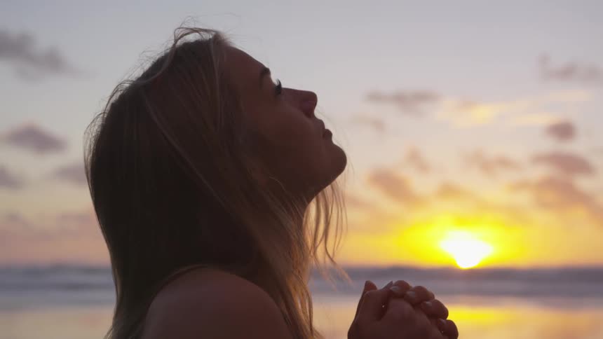 Young lady clasps her hands as in prayer and looks up to the sky
