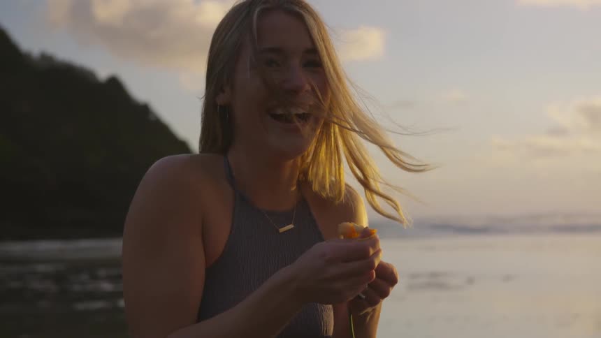 A woman standing on a beach laughing while holding a flower