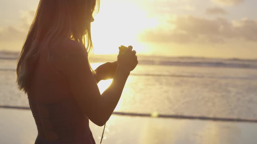 White woman stripping a flower next to the ocean at the beach