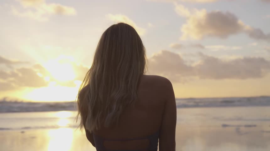 A woman in the beach looking at the sunset