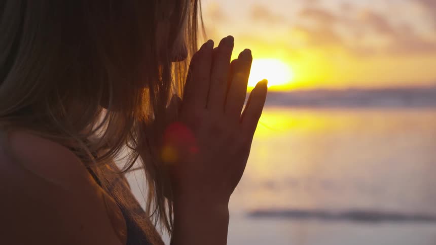 Woman praying on the beach in the middle of the sunset