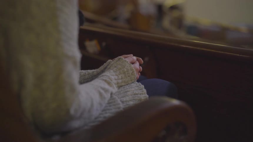 Woman sitting in church pew with hands folded