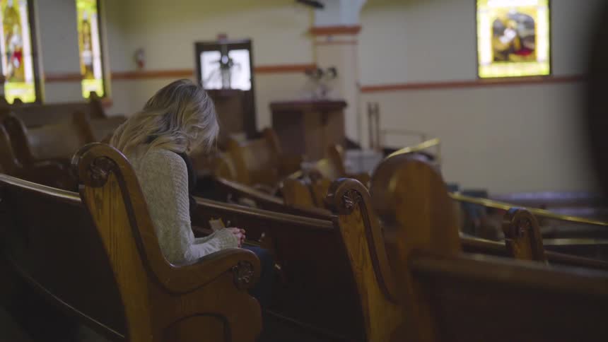 Woman sits and prays in a church pew