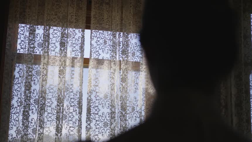 A silhouetted figure stands in front of a window